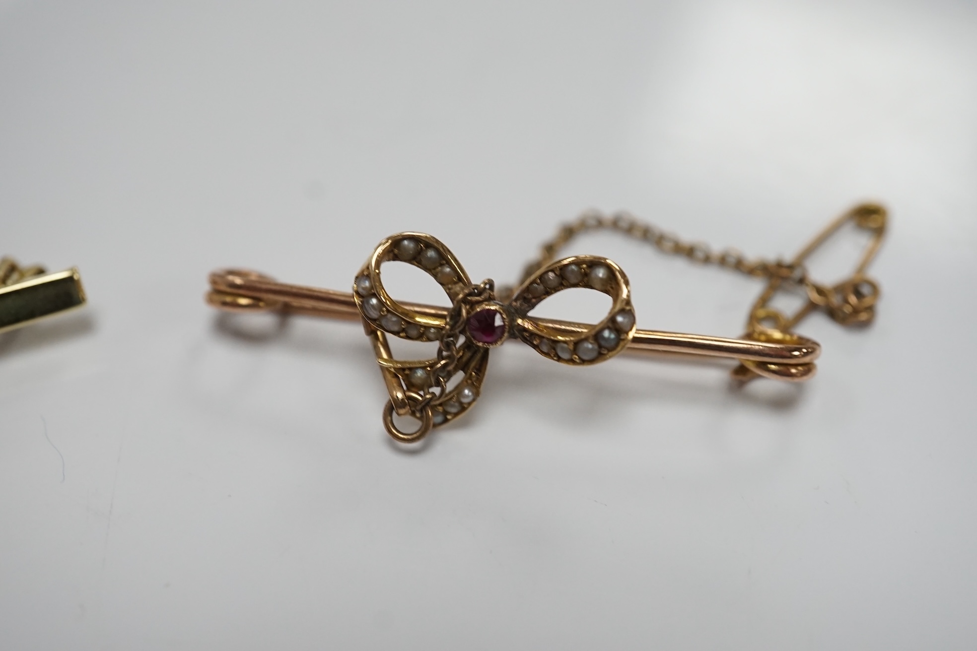 An early 20th century 15ct and solitaire diamond set bar brooch, 44mm, gross 3.5 grams and a similar 15ct, ruby and seed pearl set ribbon bow bar brooch, 2.4 grams. Condition - fair to good